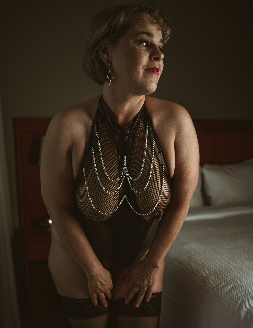 Figure in vintage-style boudoir pose wearing pearl body jewelry in moody lighting against dark background.