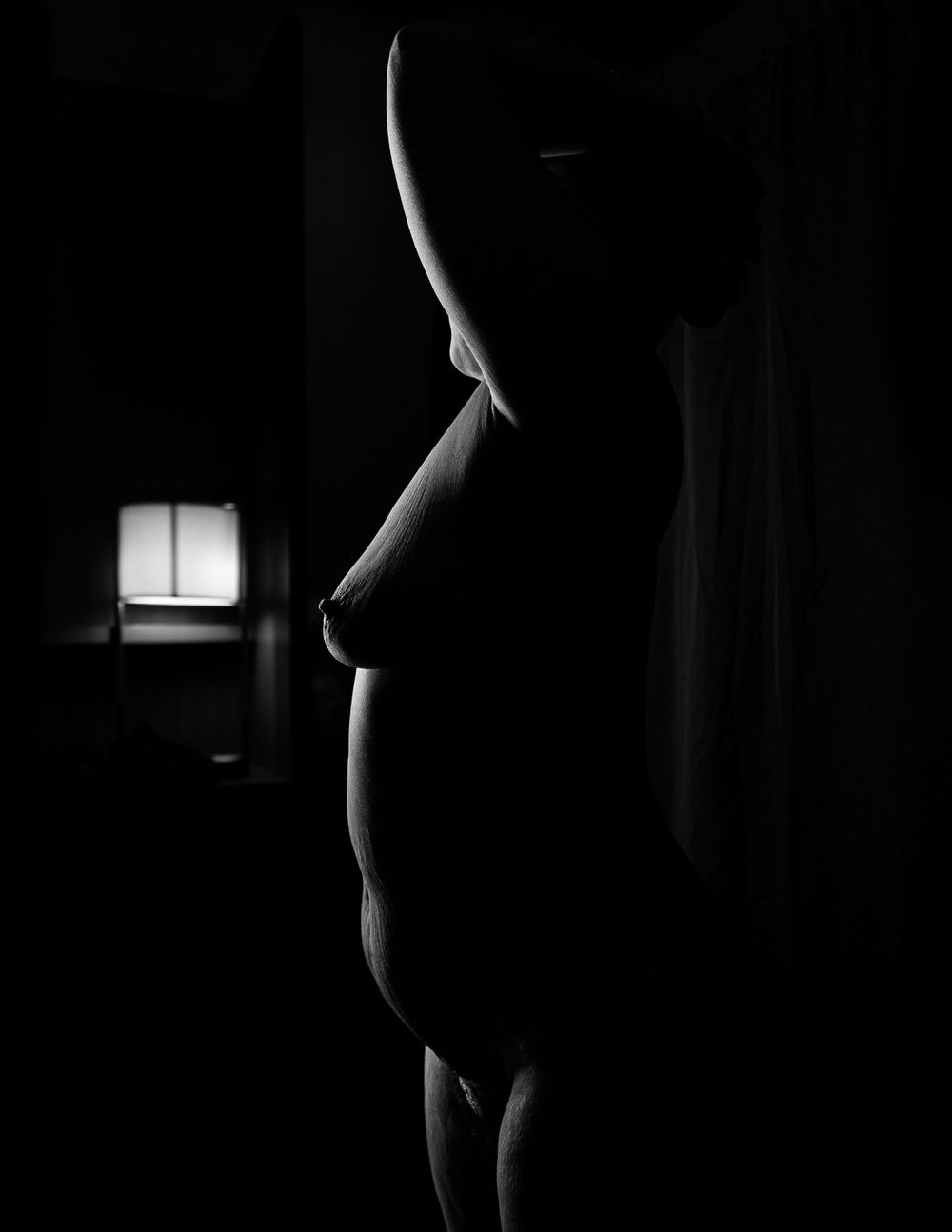 A dramatic black and white silhouette in profile against dim lighting with a small illuminated window in the background.