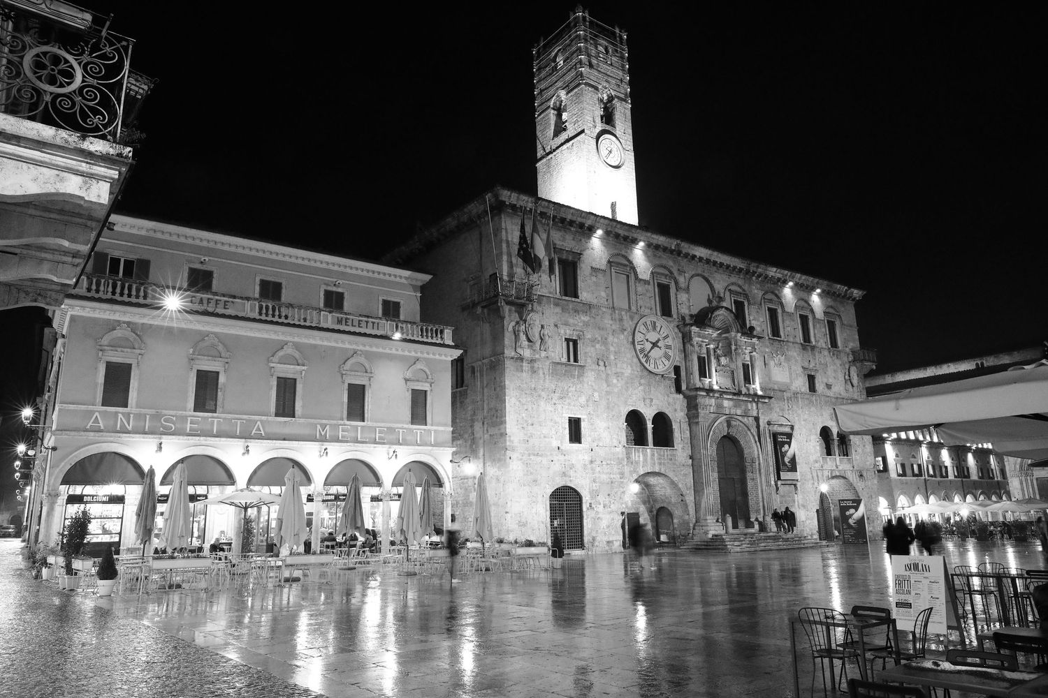 Night view of illuminated Palazzo dei Priori in black and white with wet reflective plaza.