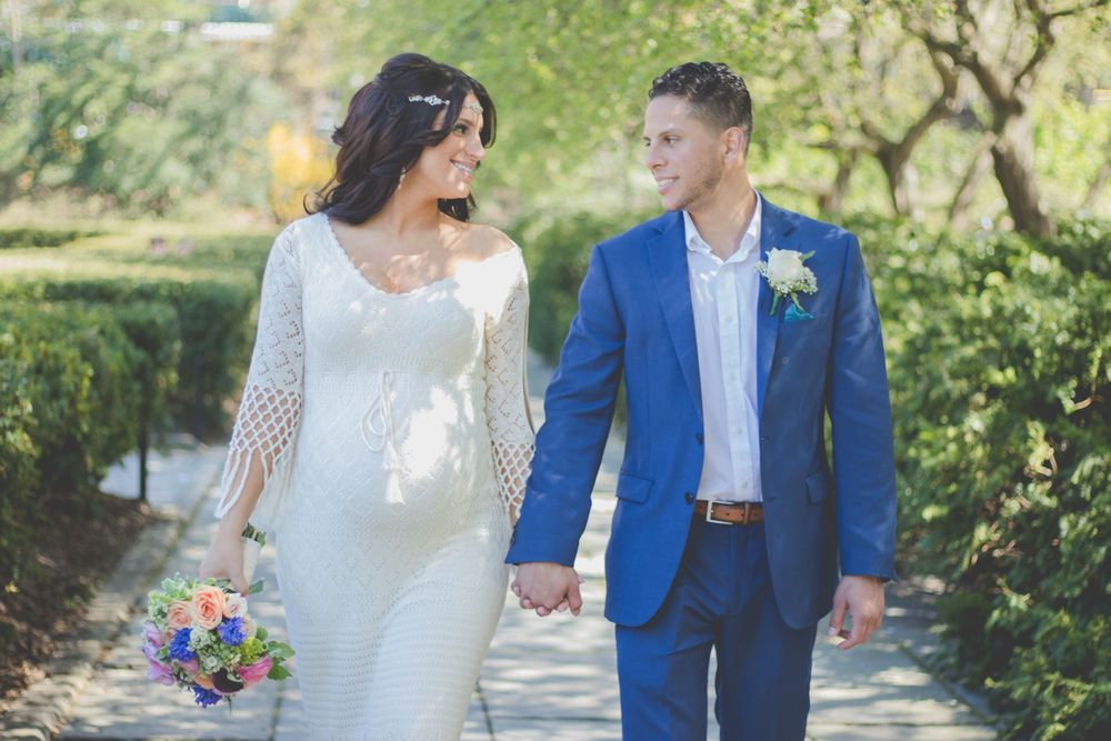 A romantic wedding couple in blue and white attire poses together in a lush garden setting.