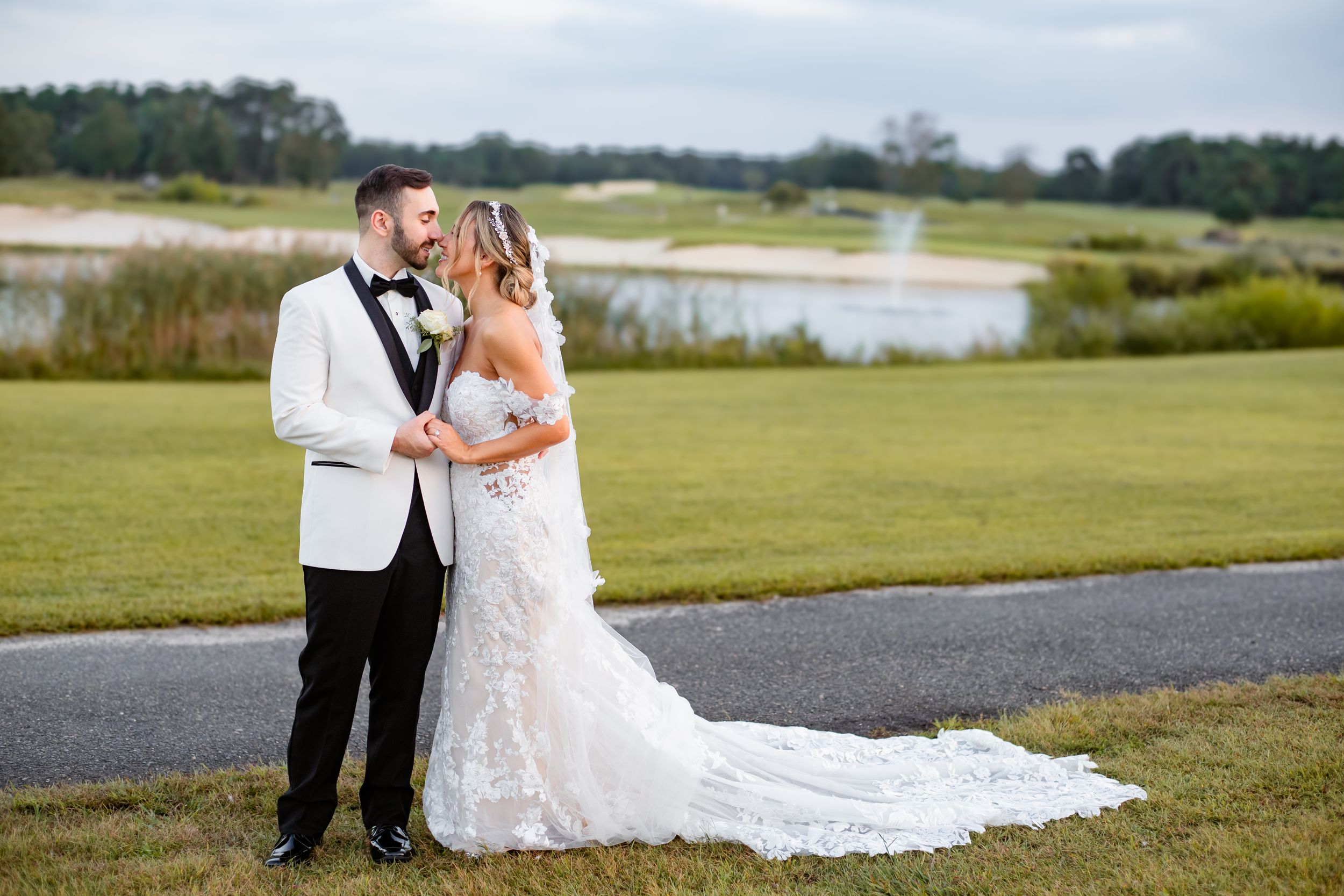 A wedding couple poses on a golf course with marshland and water features in the background.