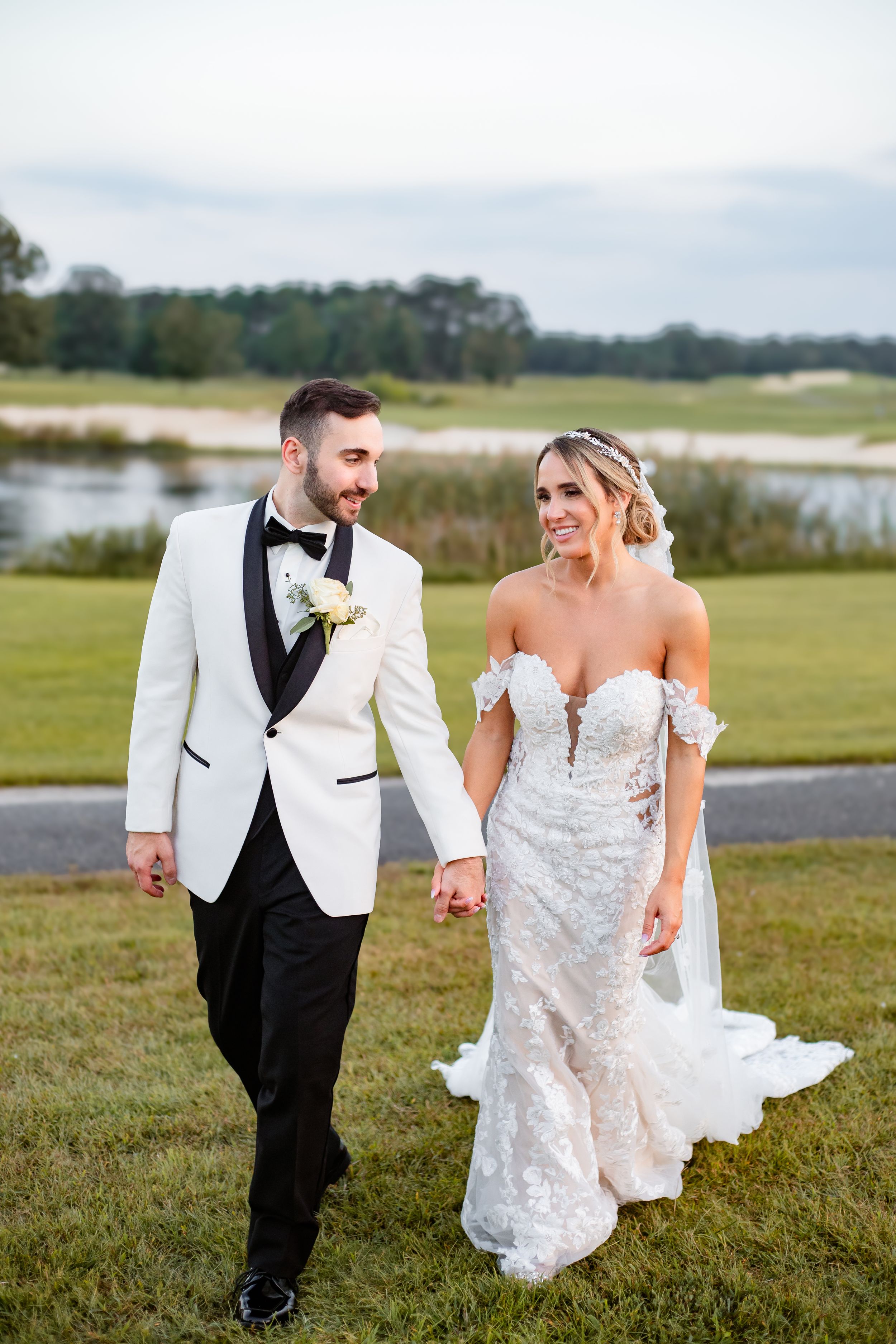 Couple walking and laughing together on a grassy field during their wedding day celebration.
