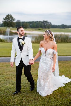 Newlyweds sharing a joyful moment while walking on green grass near a lake.