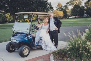Wedding couple posing with vintage golf cart on lush green golf course.
