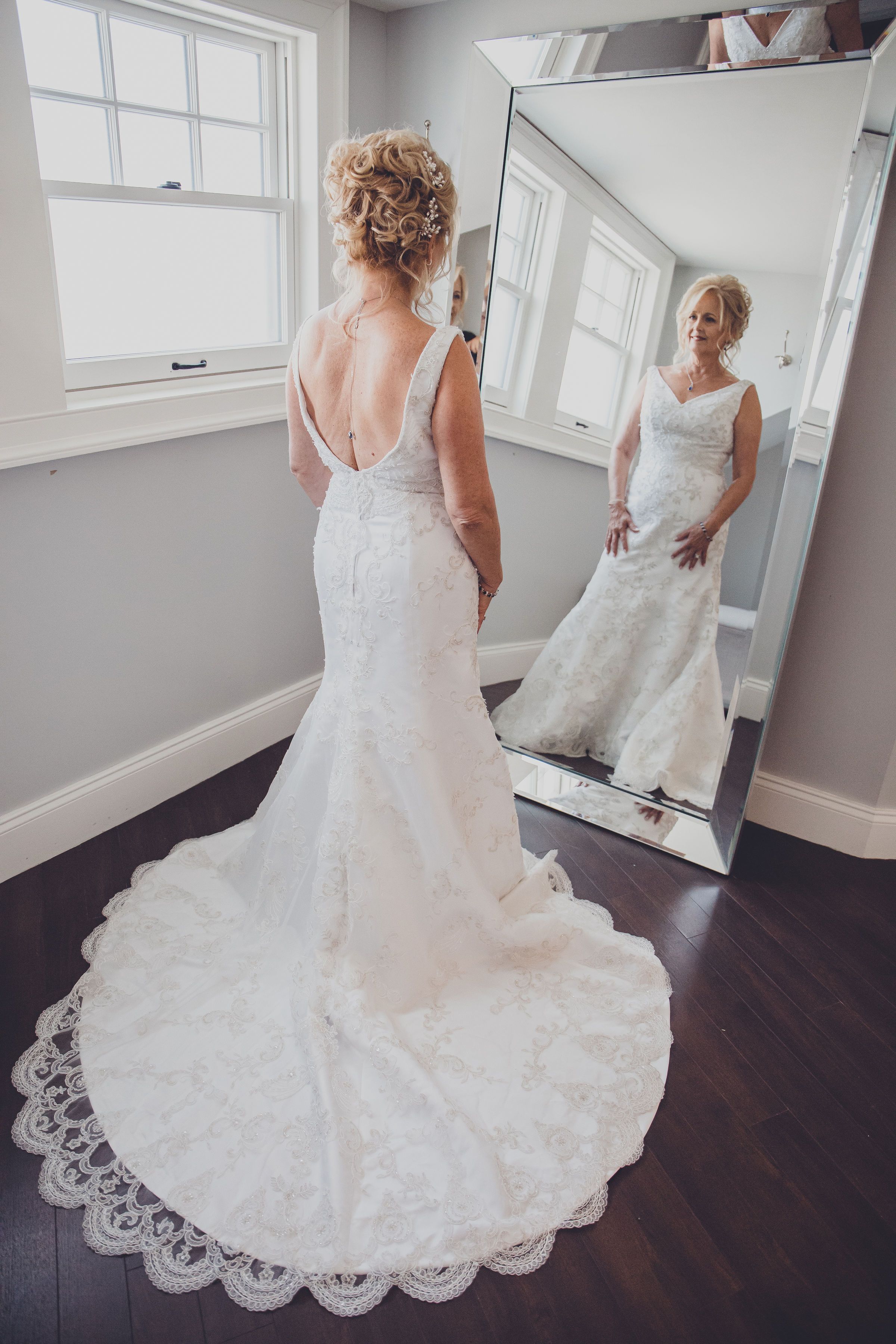 Wedding dress with intricate lace detail and long train displayed on dark hardwood floor.