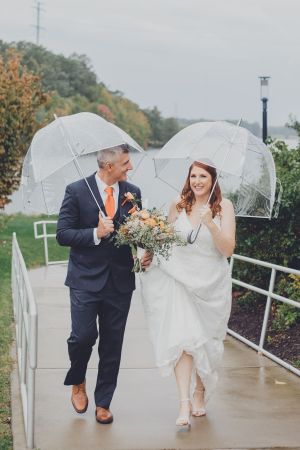 Wedding couple sheltering under clear umbrellas on a rainy day.