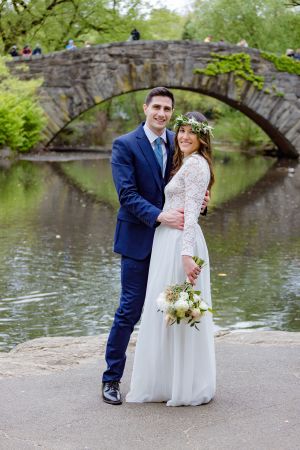 Wedding couple posing by a stone bridge over a serene pond in a park setting.