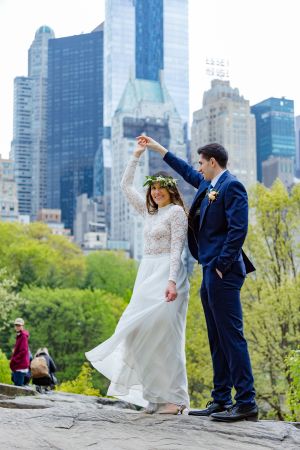A couple in wedding attire dancing on rocks in Central Park with Manhattan skyscrapers in the background.
