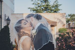 Romantic wedding couple sharing a tender moment under a white veil in an outdoor garden setting.