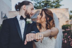 Close-up wedding ring detail shot with couple embracing in soft focus background.