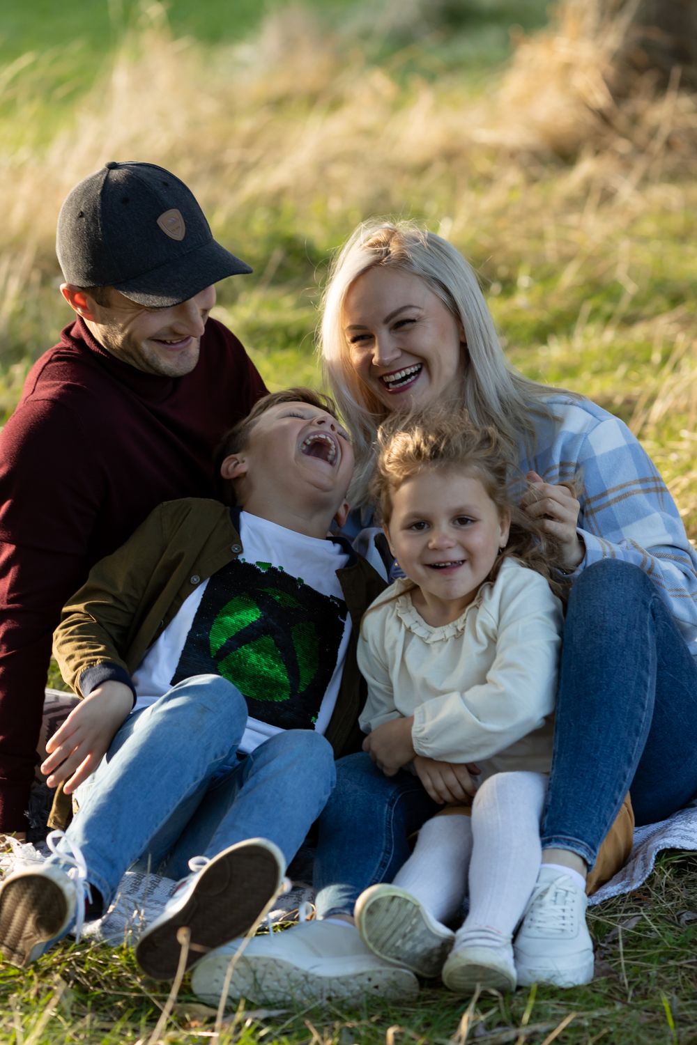 Family sharing laughs while sitting together on blanket in grassy field.