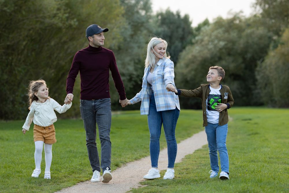 Family takes leisurely walk together on grass path through park.