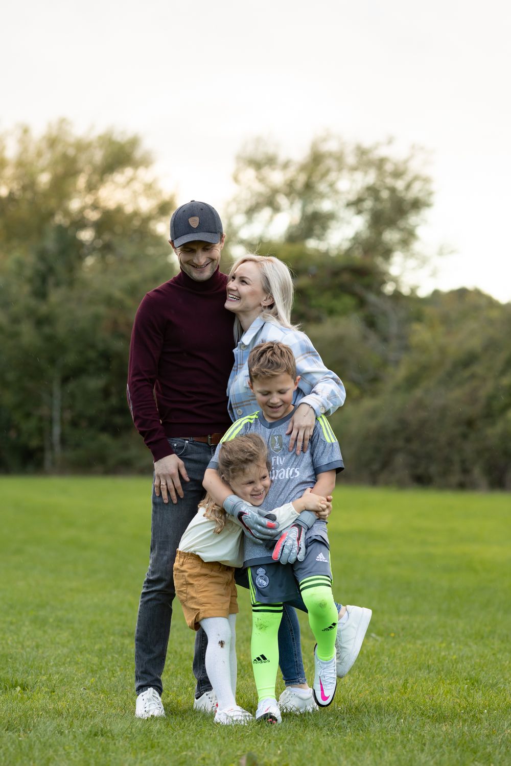 A family of four poses together on a grassy field during golden hour wearing casual fall attire.
