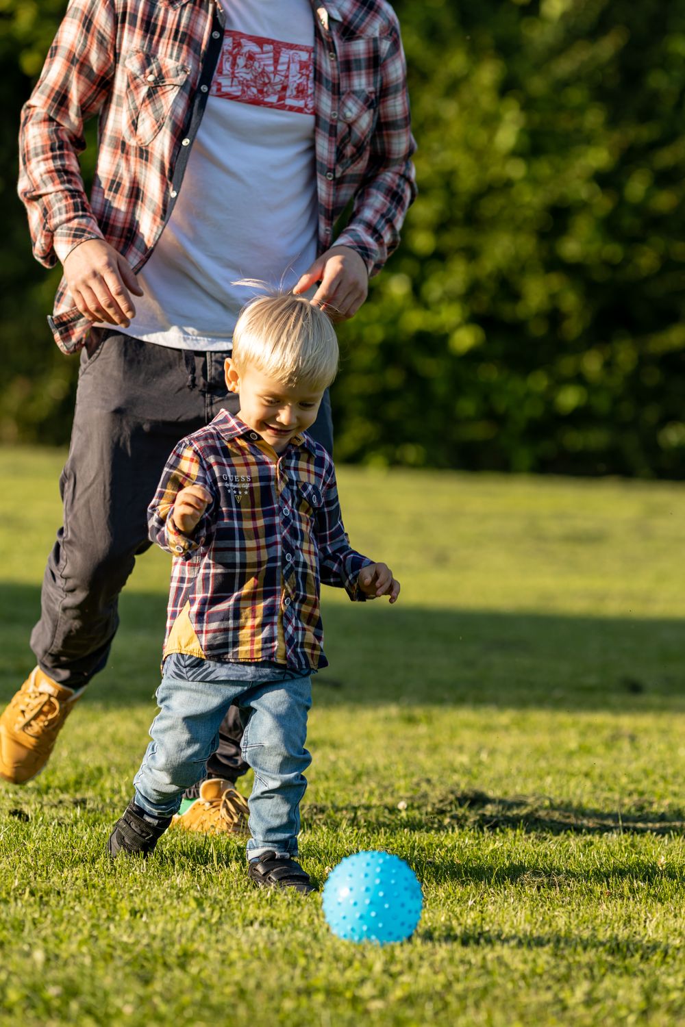 Toddler playing soccer with blue ball on grass field.