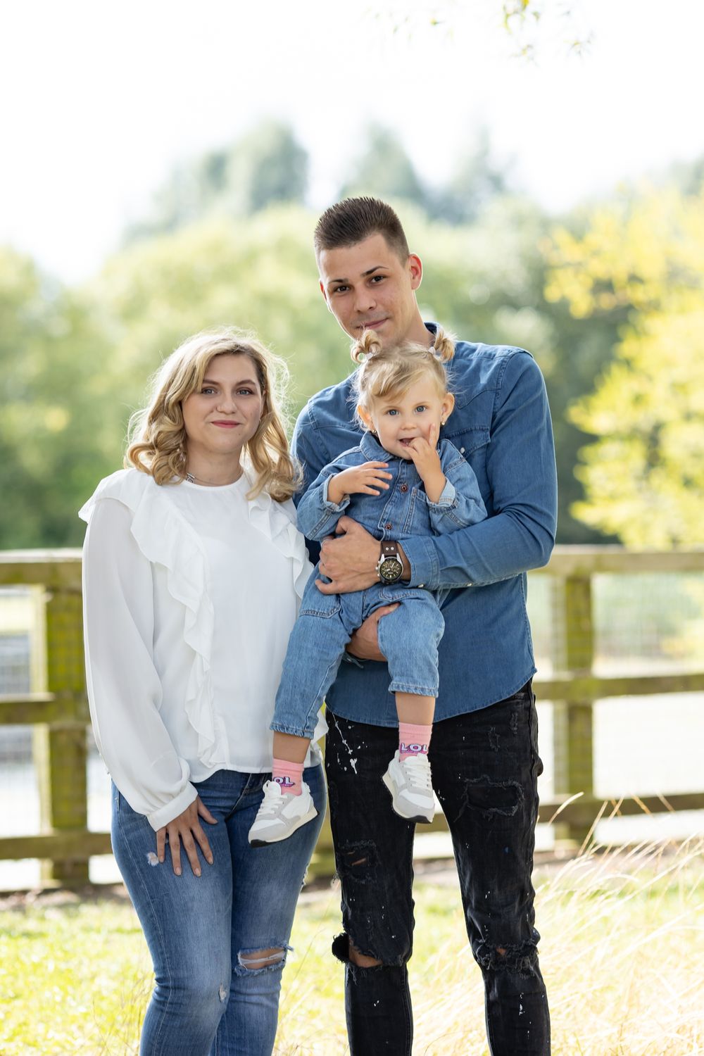 Family of three poses together on wooden bridge during autumn outdoor photoshoot.