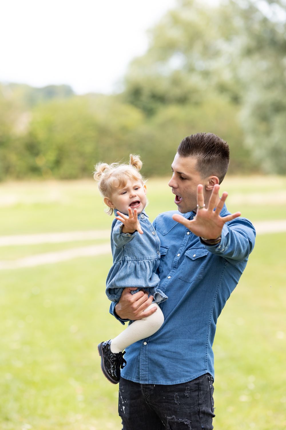 A parent and toddler share a playful moment outdoors while wearing matching blue outfits.
