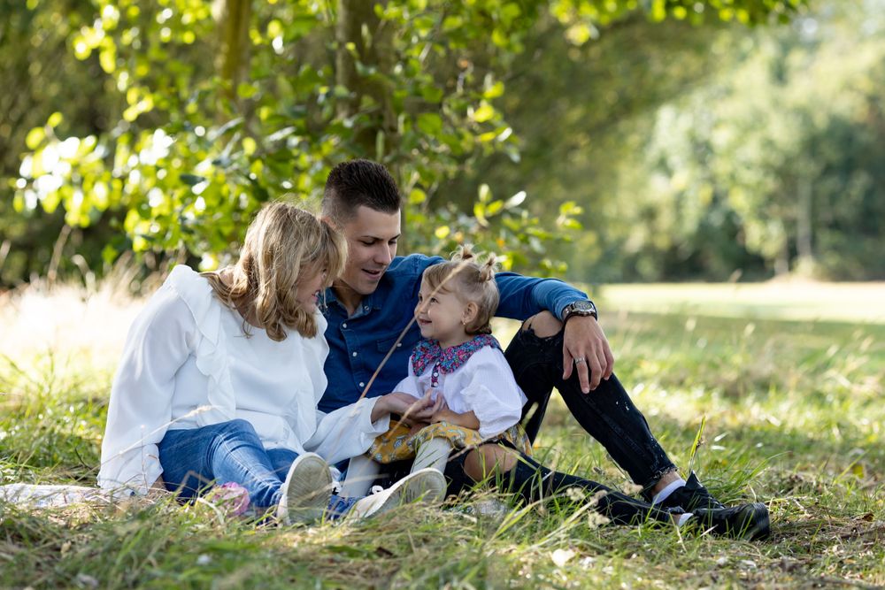 Family relaxes together on grassy hill during outdoor photo session.