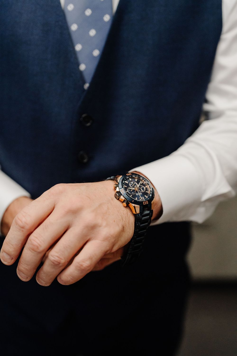 Close-up of a formal outfit featuring a navy vest and white dress shirt with an elegant wristwatch on display.