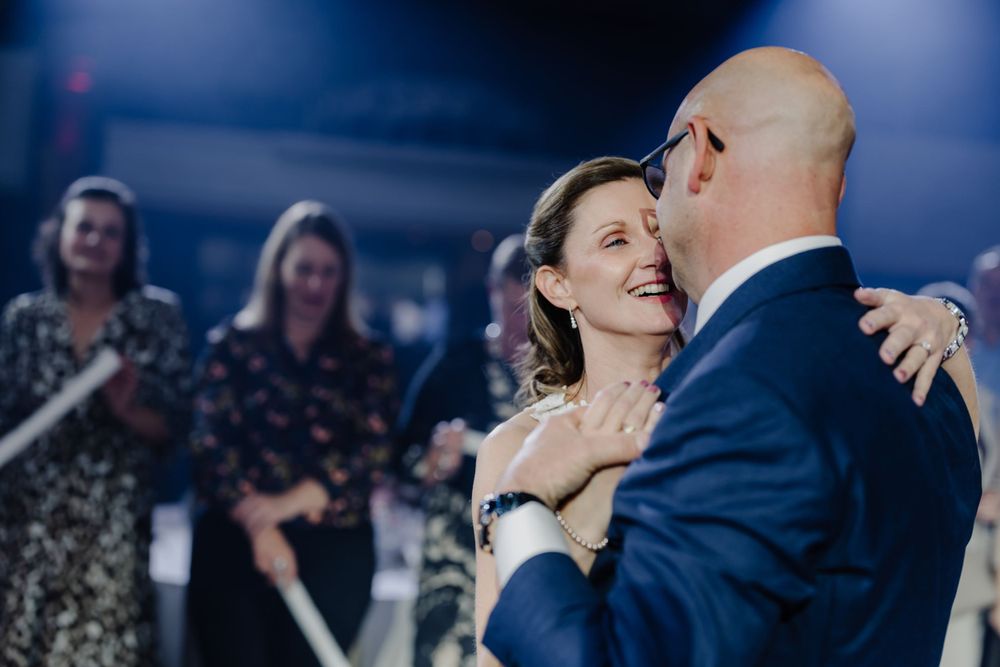 A couple shares their first dance at a wedding reception while guests watch in the background.