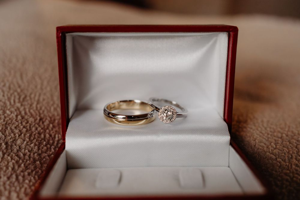 Wedding rings resting in a red velvet jewelry box with a gold band and diamond engagement ring.