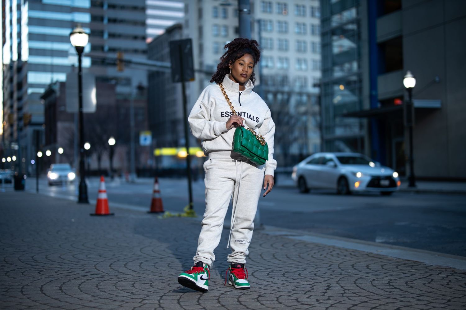 Street style photo of person in white Essentials tracksuit and green bag against urban backdrop.