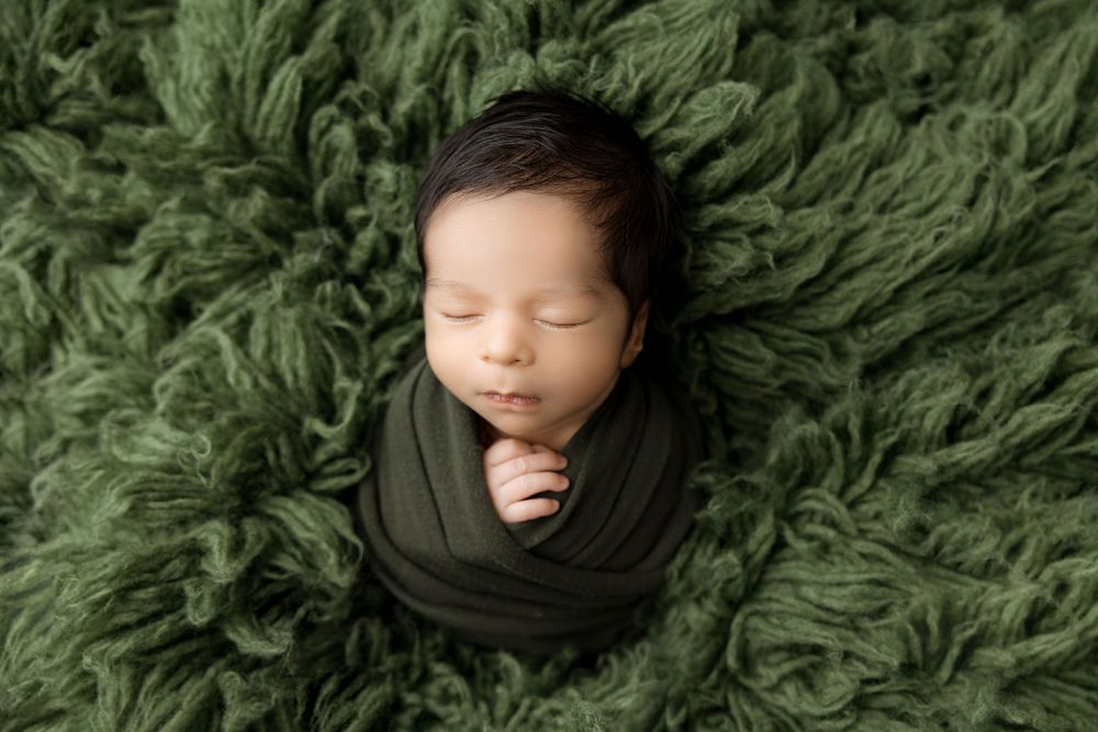 Newborn flokatti pose on green set up and wrapped baby.