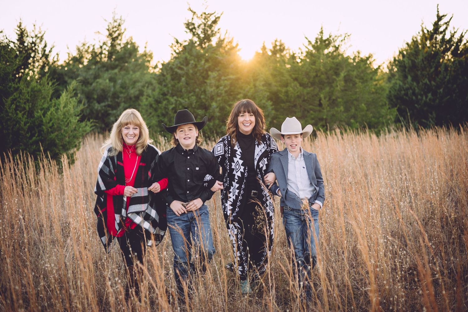 A group stands together in a field of tall grass at golden hour with evergreen trees in the background.