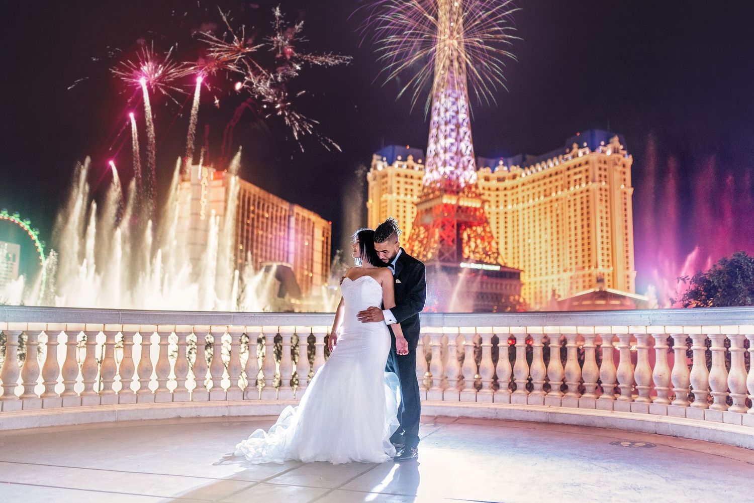 Romantic wedding couple silhouetted against Bellagio fountains and Las Vegas lights with fireworks in background.