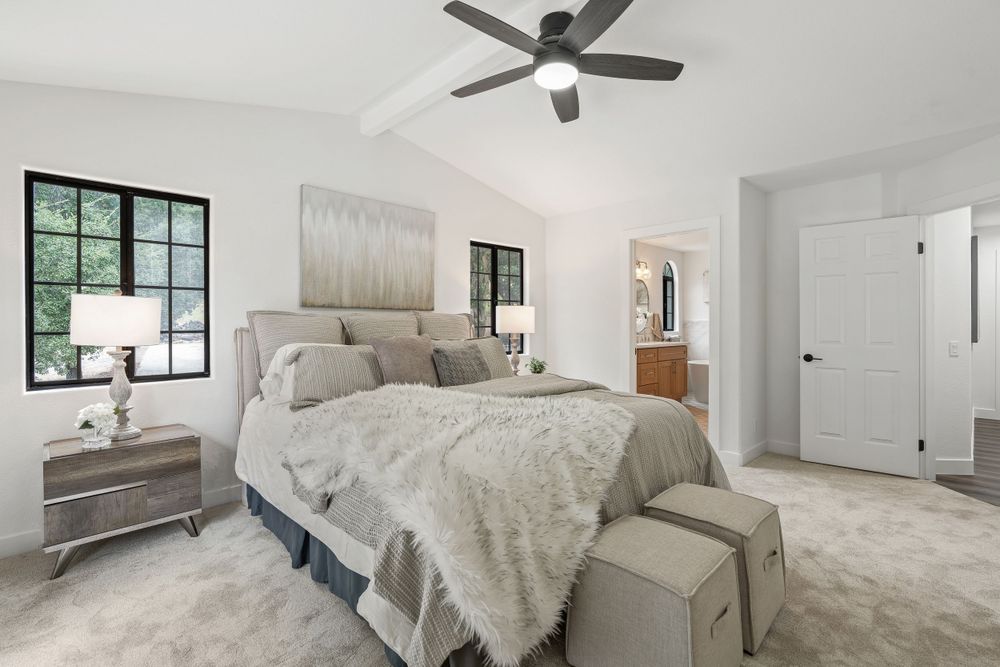 Modern bedroom featuring plush bedding, ceiling fan, and black-framed windows with natural light.