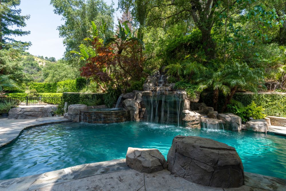 Luxury backyard pool with rock waterfall features and lush landscaping in natural setting.
