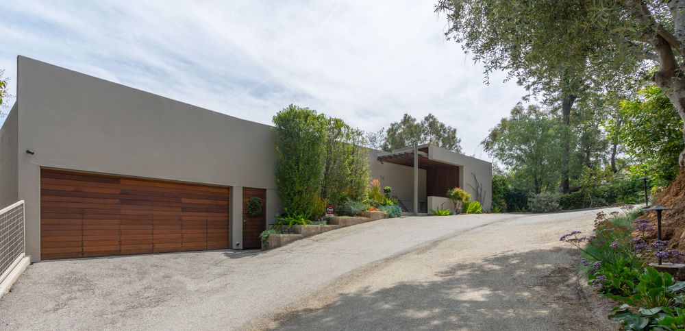 Modern hillside home with angular architecture and wooden garage door on sloped driveway.