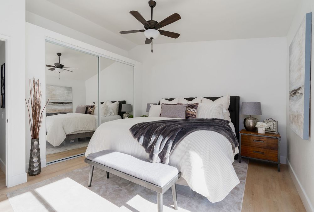 Contemporary bedroom with mirrored closet doors, gray bedding, and ceiling fan.