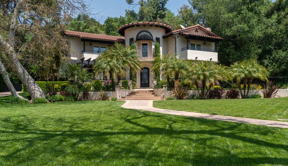 Mediterranean style mansion with arched entrance and palm trees on manicured front lawn.