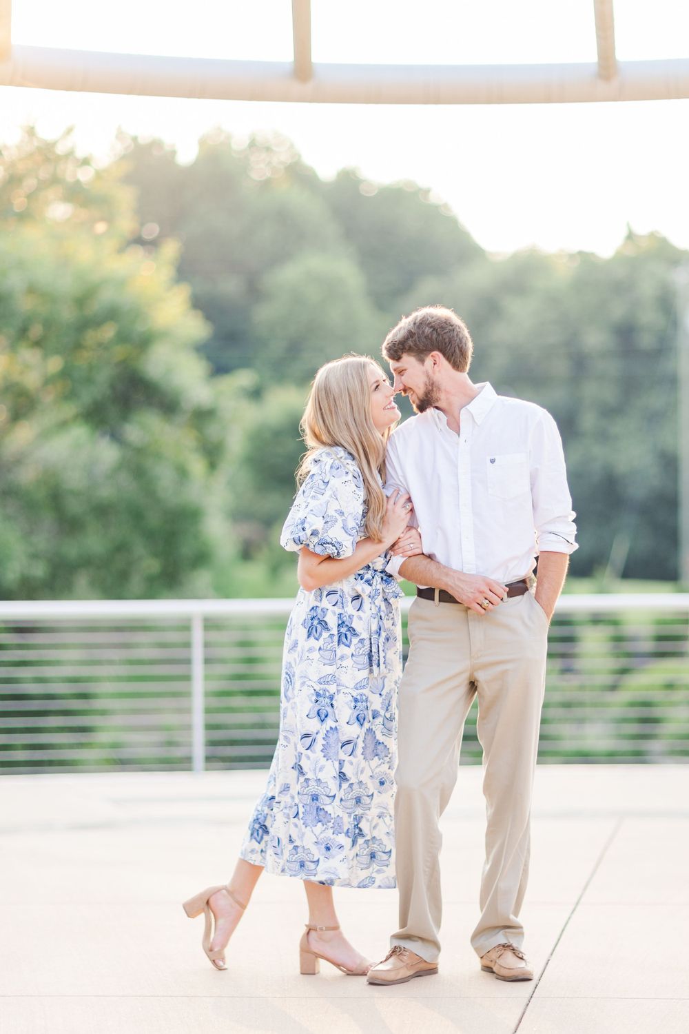 Romantic couple in blue floral dress and white shirt sharing tender moment on terrace.