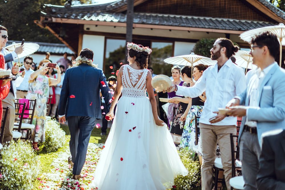 Wedding guests celebrate as newlyweds walk down a garden path at an Asian-inspired venue.