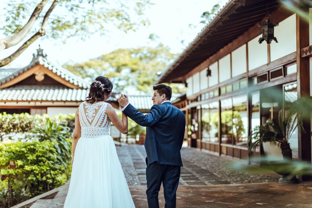 Newlyweds dance together outside a traditional Asian-style building.