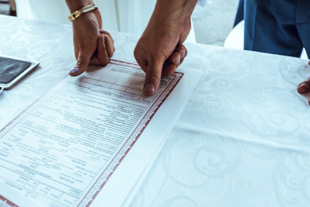 Close-up of hands signing wedding documents on a white tablecloth.