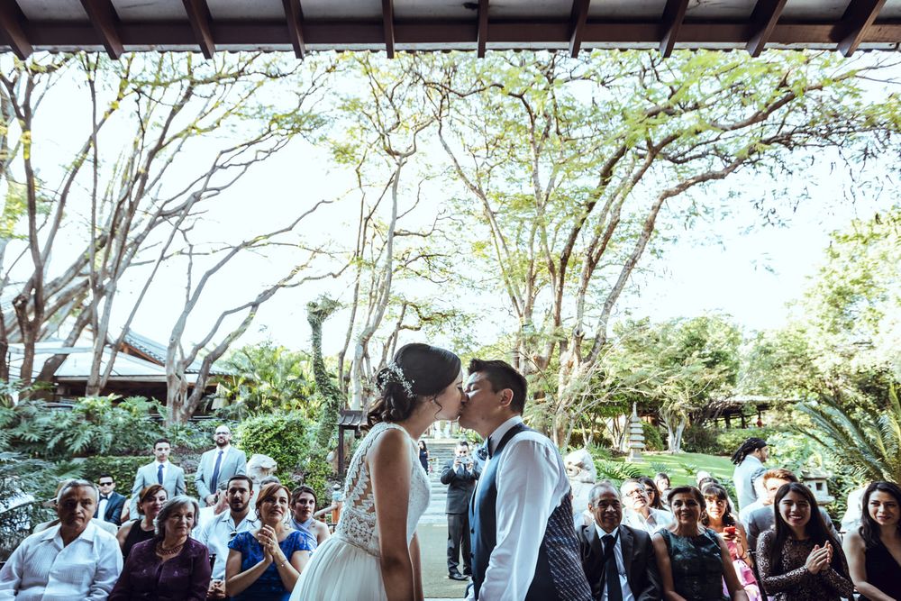 Outdoor wedding celebration at a covered Japanese pavilion surrounded by trees.