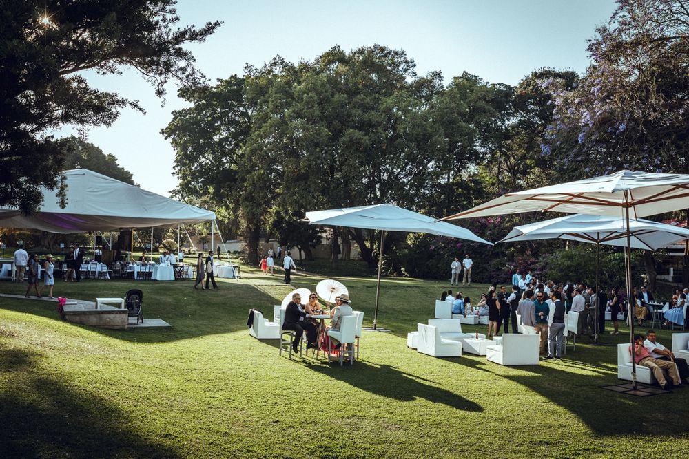 Wide panoramic view of a sunny outdoor wedding reception venue with umbrellas and tents.