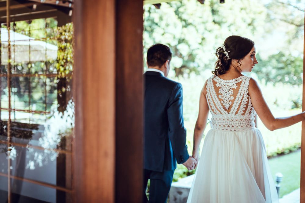 Wedding couple standing at a venue entrance with greenery in the background.