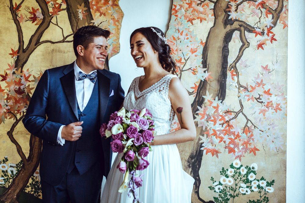 Couple in wedding attire posing against wall with painted cherry blossom tree mural.