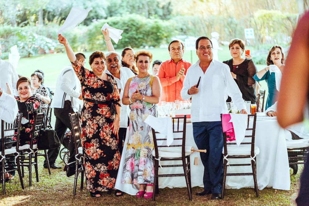 Wedding guests celebrate joyfully outdoors under a canopy with floral decorations and white chairs.