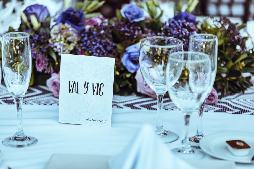 Table setting with wine glasses and floral centerpiece featuring purple blooms on patterned tablecloth.