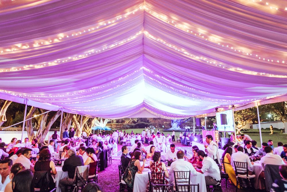Large wedding reception tent illuminated with purple lighting and string lights over dining tables.