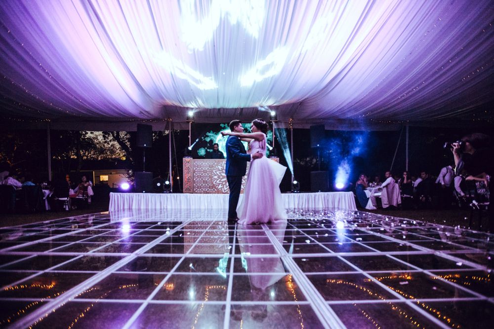 Evening wedding reception with illuminated dance floor under draped fabric ceiling.