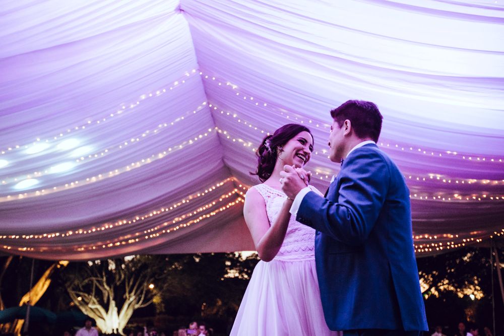 Romantic dance under draped fabric ceiling with twinkling lights at wedding reception.