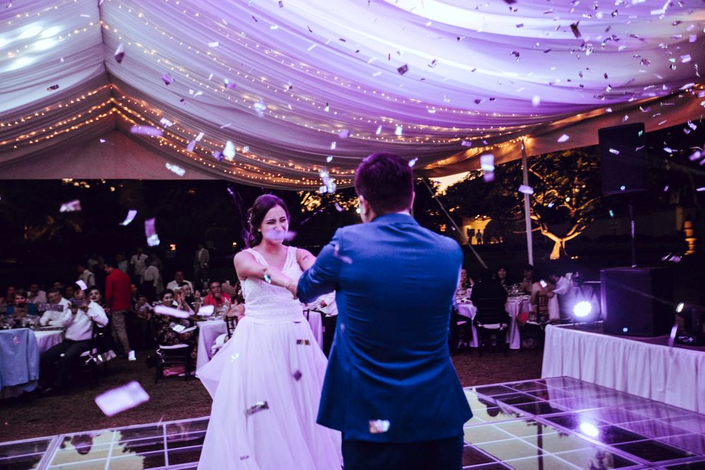 A couple shares their first dance at a wedding reception under twinkling lights and draped fabric decorations.