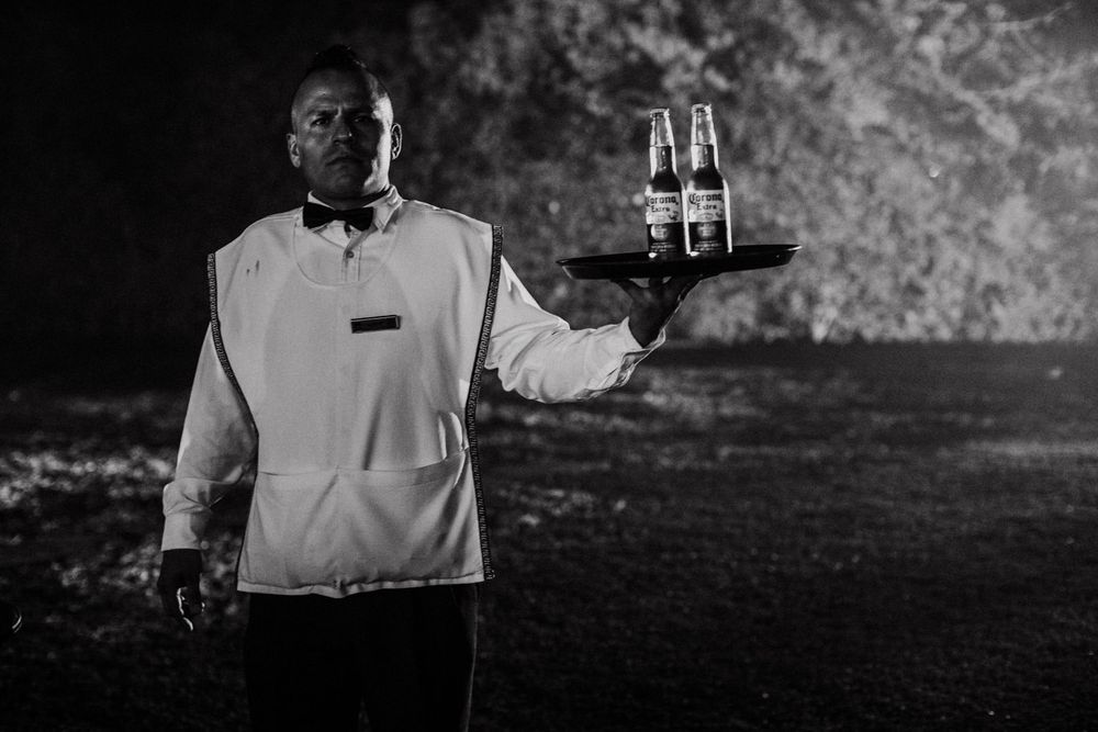 A server in formal attire holds a tray of drinks in a dramatic black and white photograph.