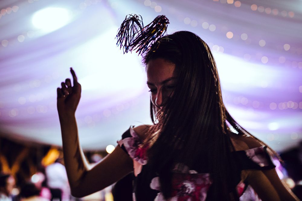 Silhouetted party guests dancing and celebrating under purple stage lighting in a festive atmosphere.
