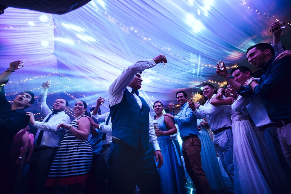 Crowd of wedding guests dancing under draped ceiling with blue uplighting in a tent venue.